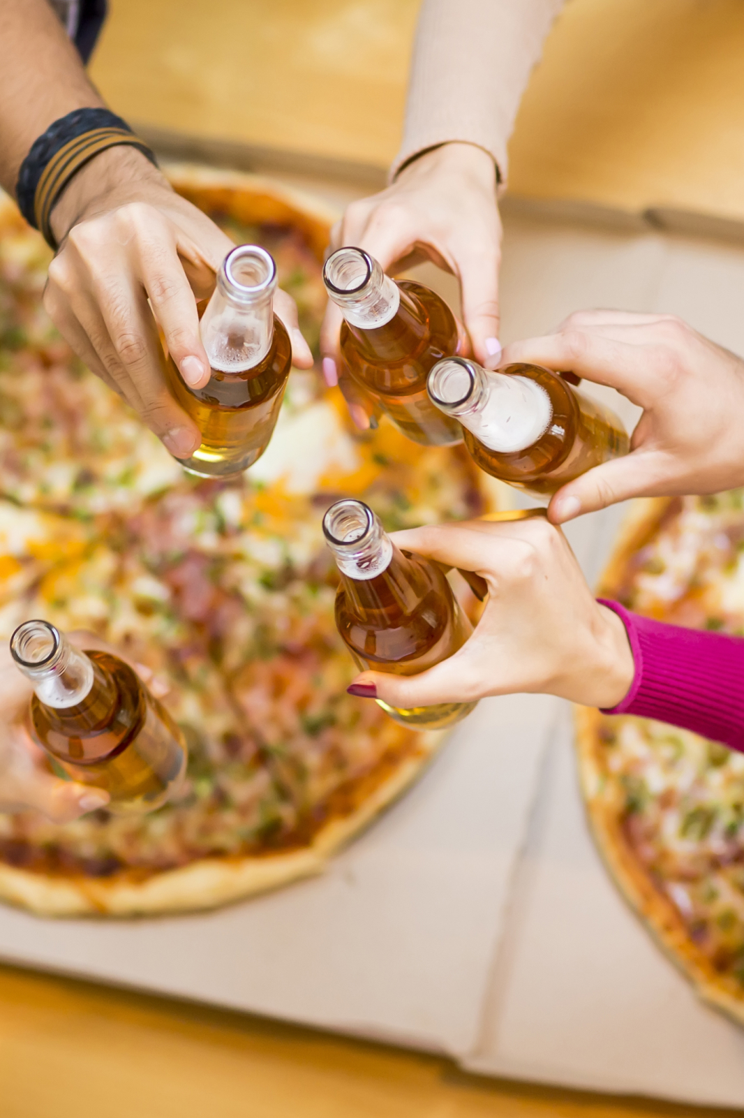 Personas brindando con botellas de cerveza sobre una pizza grande en iPizza & Burger Valladolid